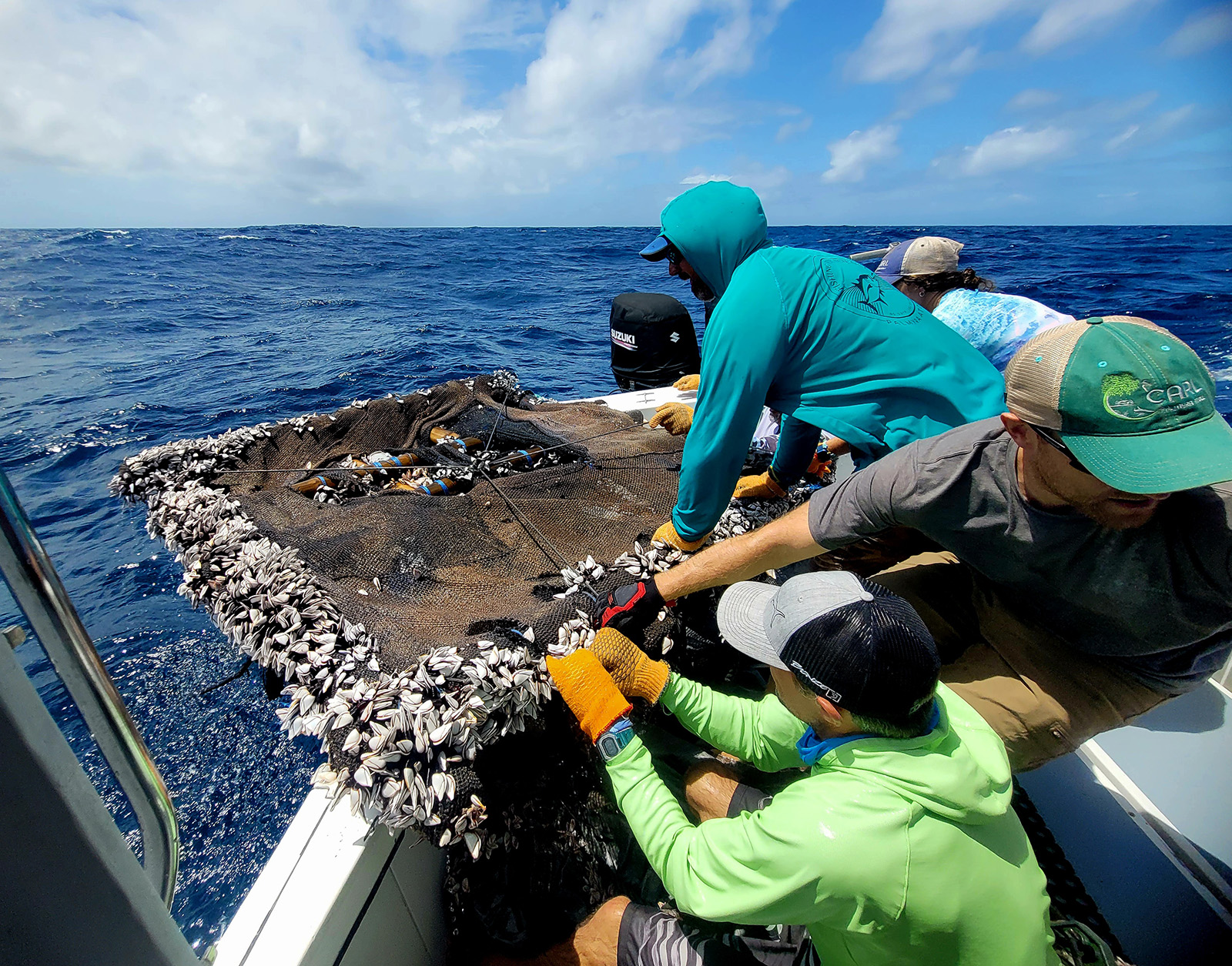 Four people on a small boat pulling a unwieldy drifting Fish Aggregation Device out of the ocean near Palmyra Atoll.