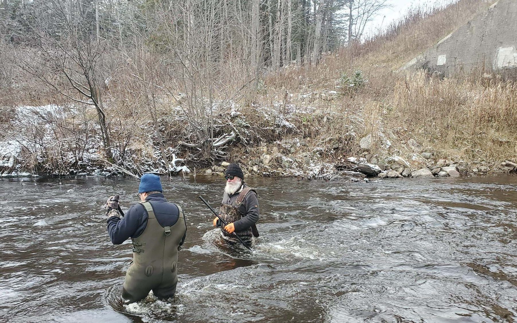 Two people wade in a river on a cold November day.