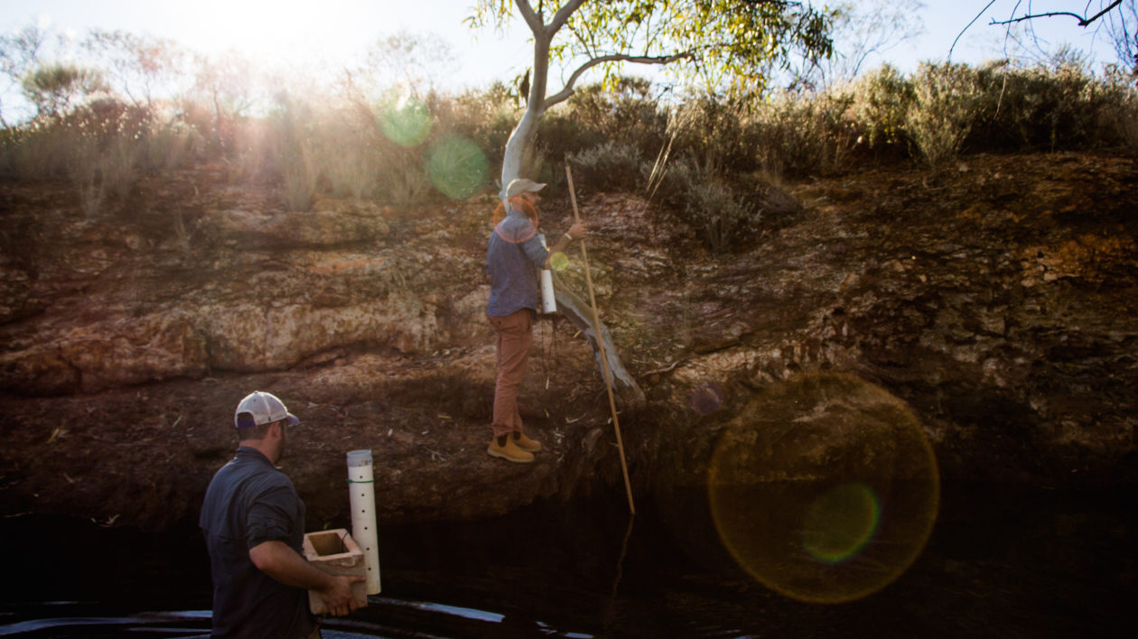 Game and O’Bryan scale a waterhole cliff with the data logger. Photo © The Nature Conservancy (Justine E. Hausheer)
