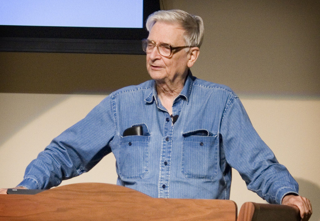 elderly man in blue shirt standing at a lectern