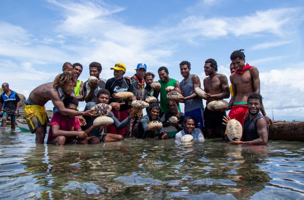 A group of men holding sea cucumbers in shallow water.