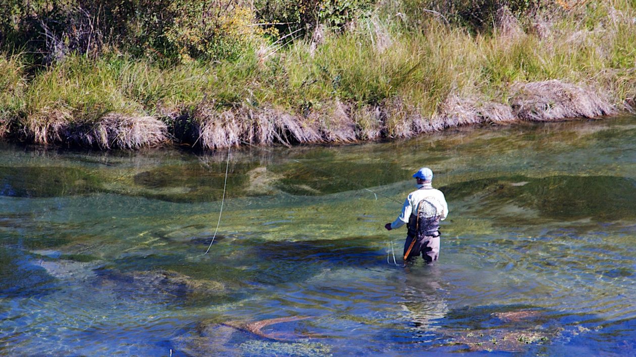 man wading into a stream to fish