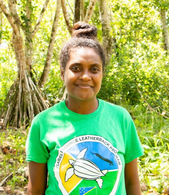 a women looking at the camera and standing in front of trees