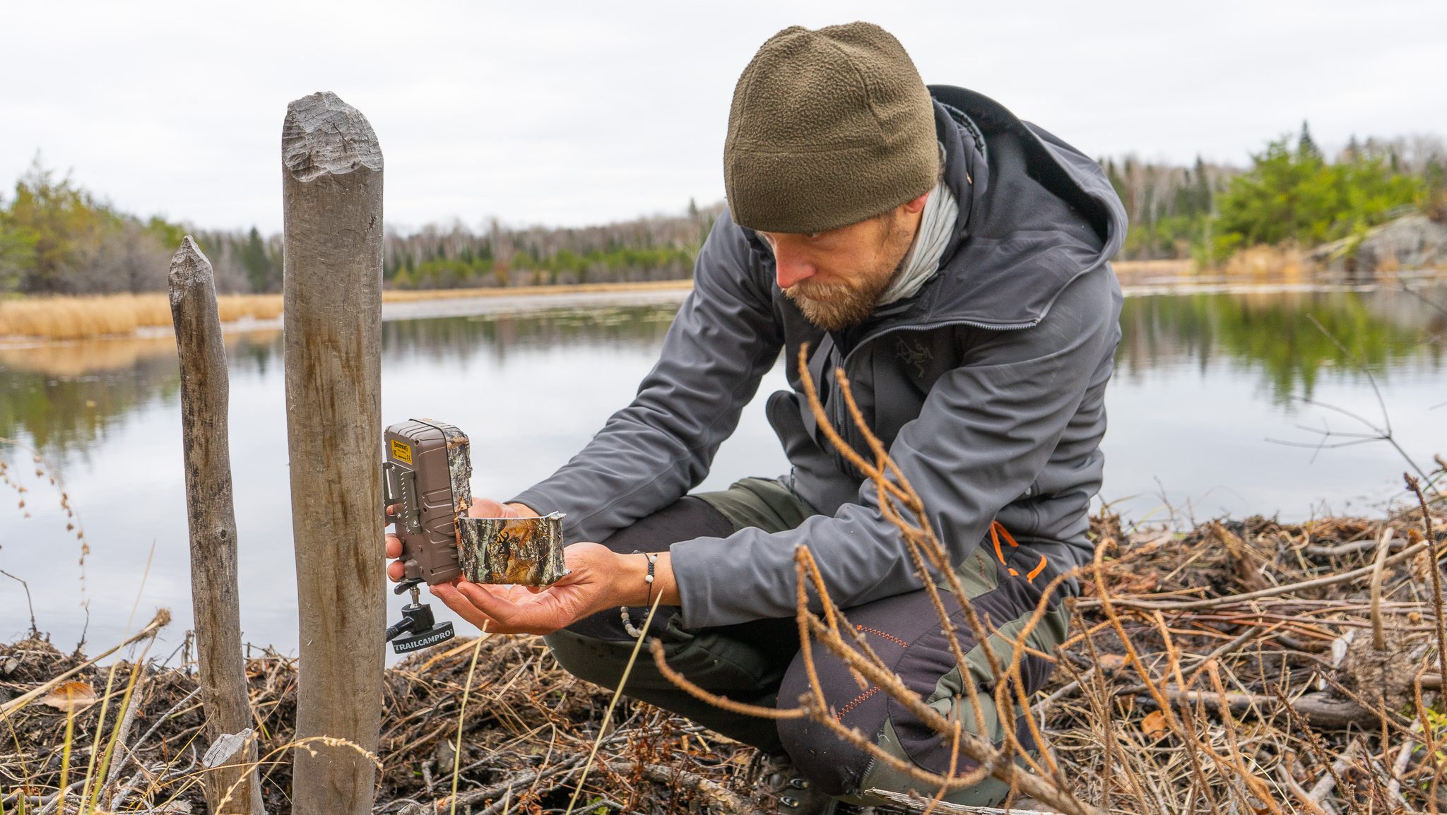 man setting up trail camera next to a pond
