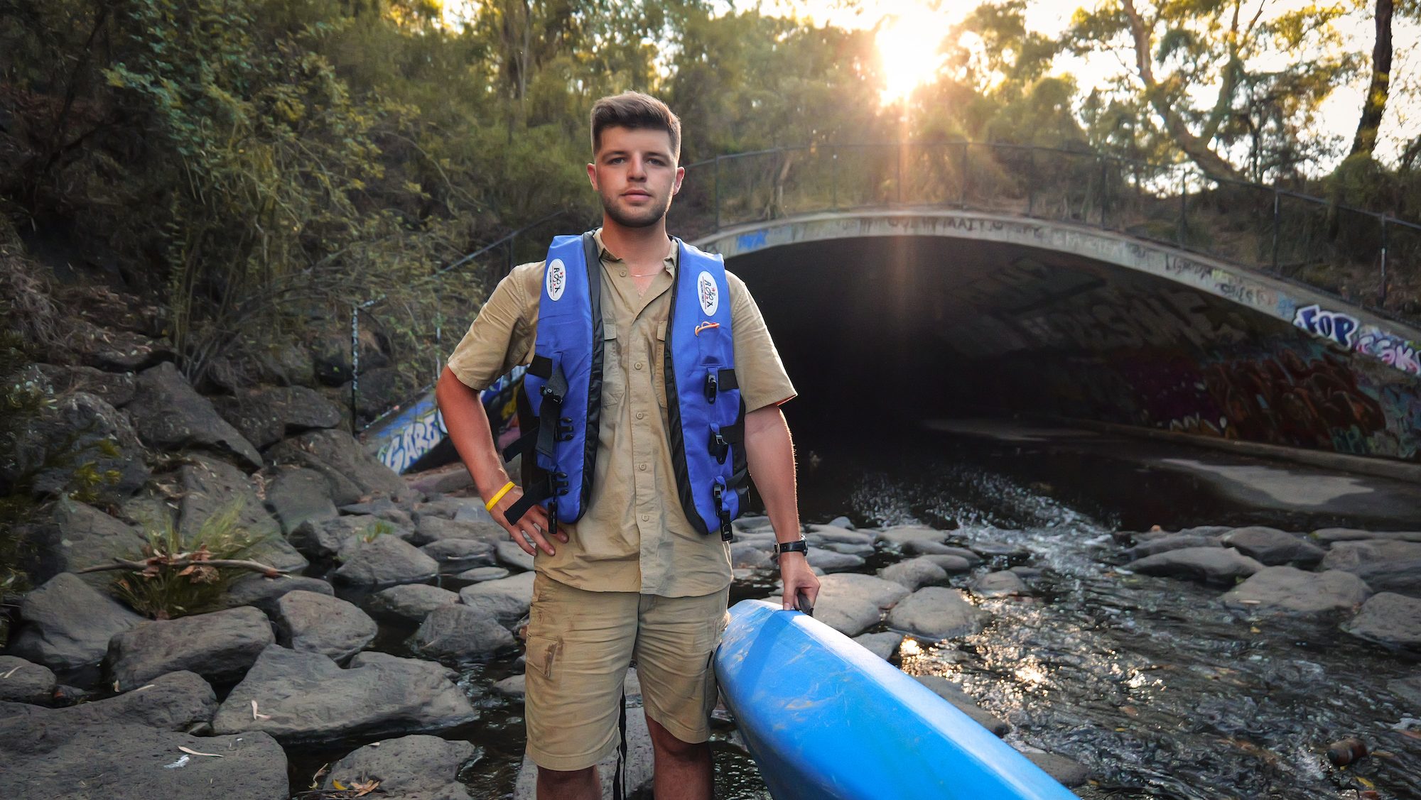 man standing in front of a storm drain holding a kayak