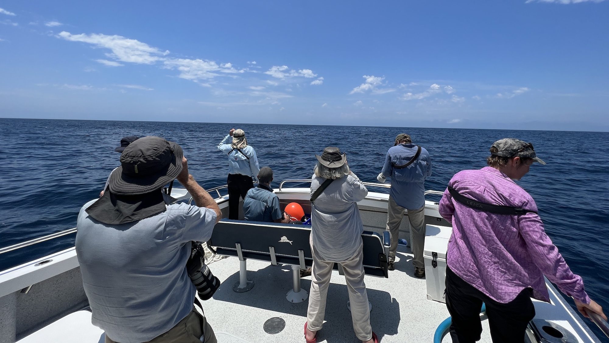 group of people standing on a boat looking out into the ocean with binoculars
