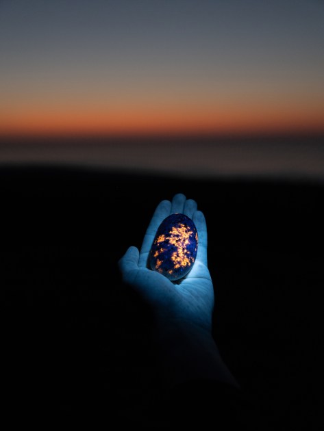 a hand holding a rock glowing under UV light g