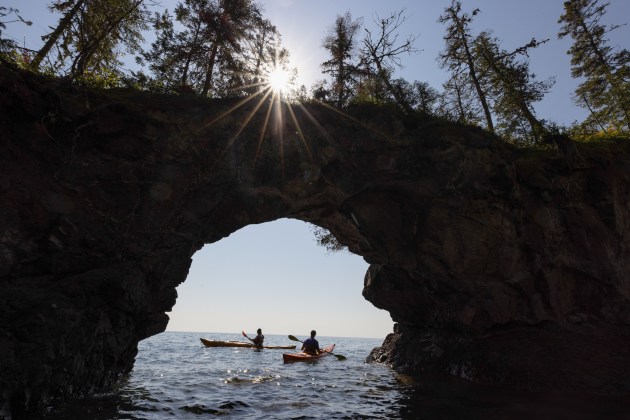 two people kayaking out to sea in front of a stone arch