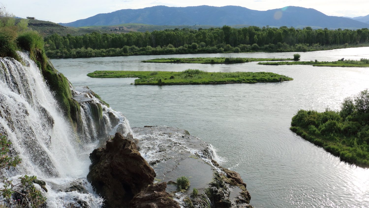 vista de una cascada y un lago con montañas en la distancia