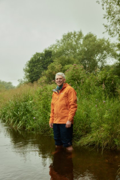 A man in an orange shirt standing in front of a river.