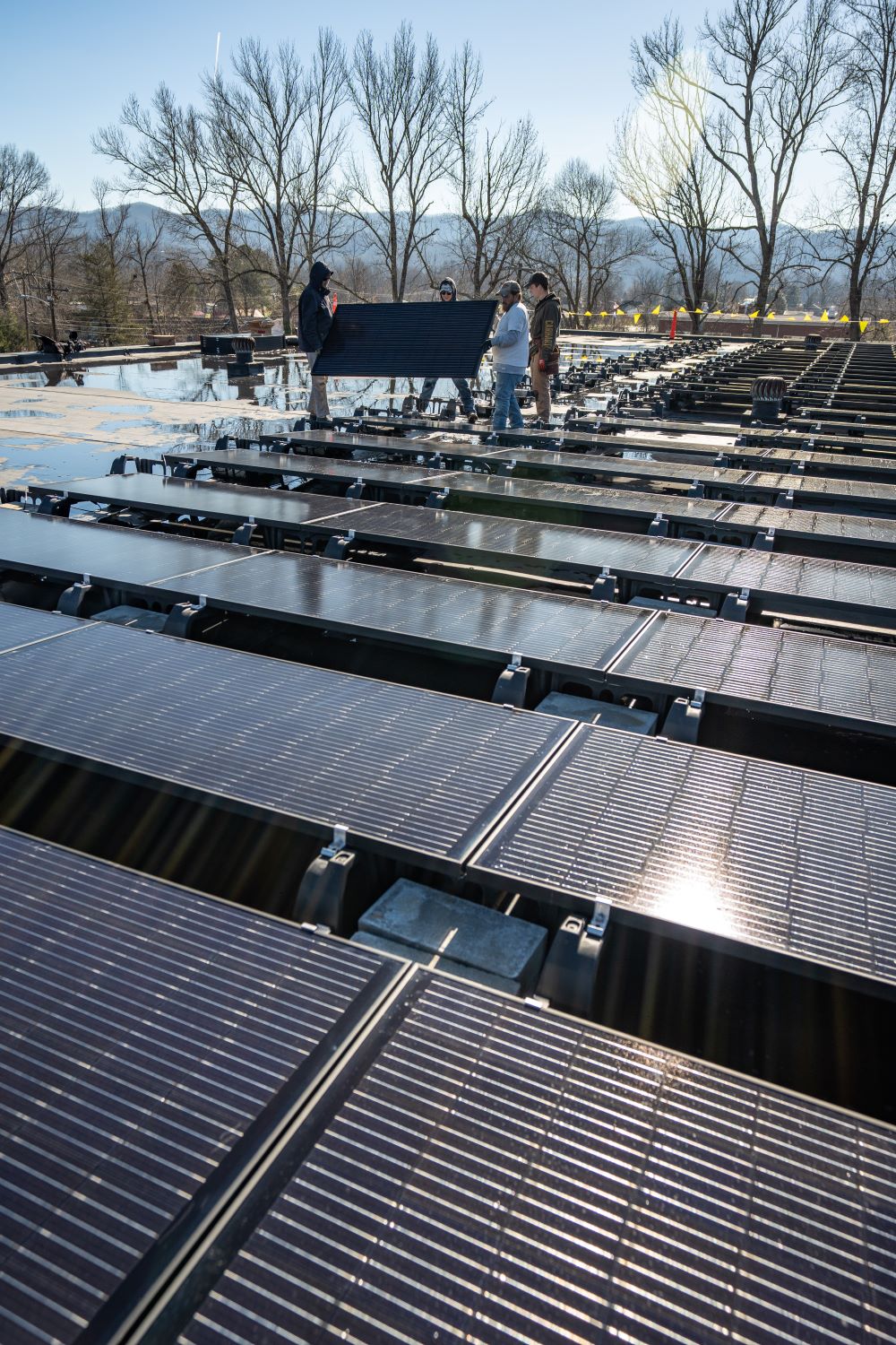 Group of workers holding a solar panel as they work to install dozens on a roof.