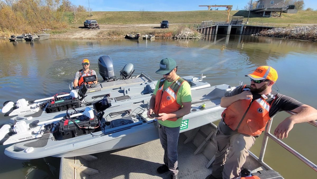 Three people standing in front of autonomy kayaks on the shoreline