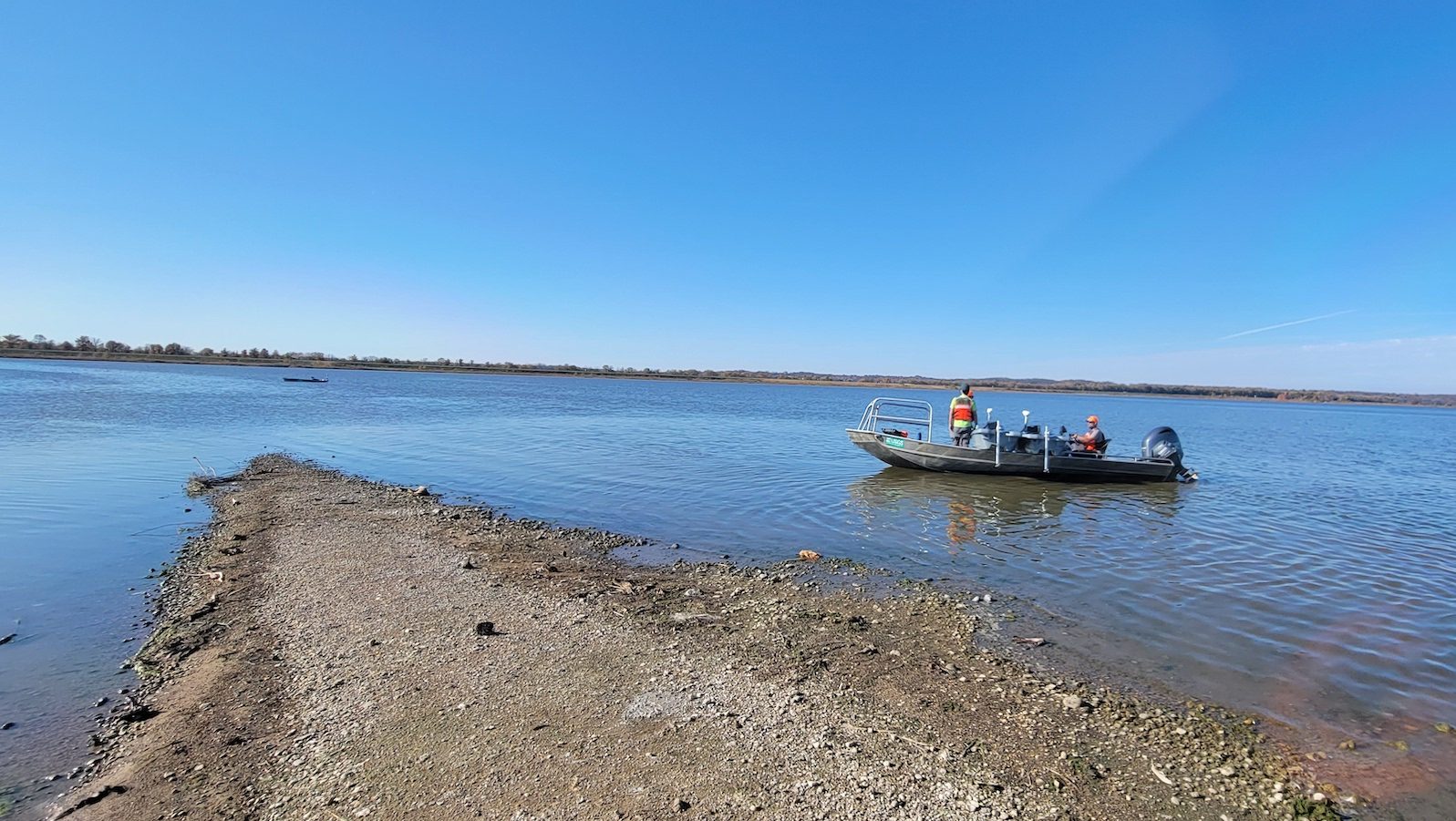 A person in a boat just offshore watches an autonomous kayak in the distance. 
