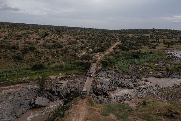 An aerial view of cars driving over a bridge that spans a rocky river. 