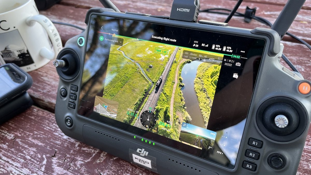 A drone controller on a table top. The screen shoes an aerial view of a hayfield.