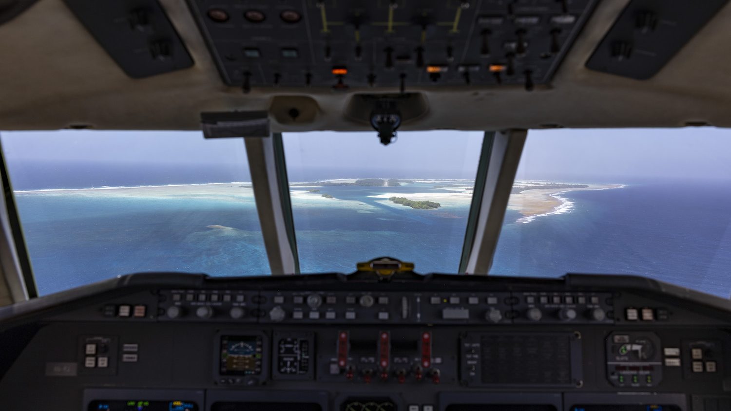 The view of a small island seen through the front window of a cockpit.