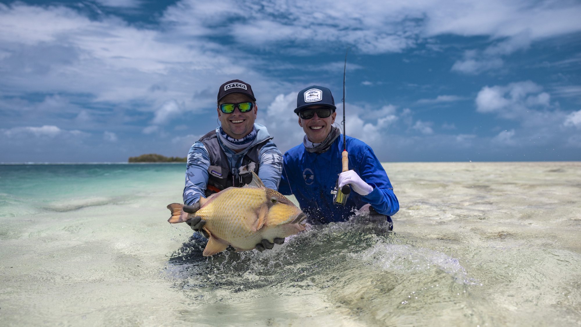 A man and a woman standing in the shallows with a very large fish.