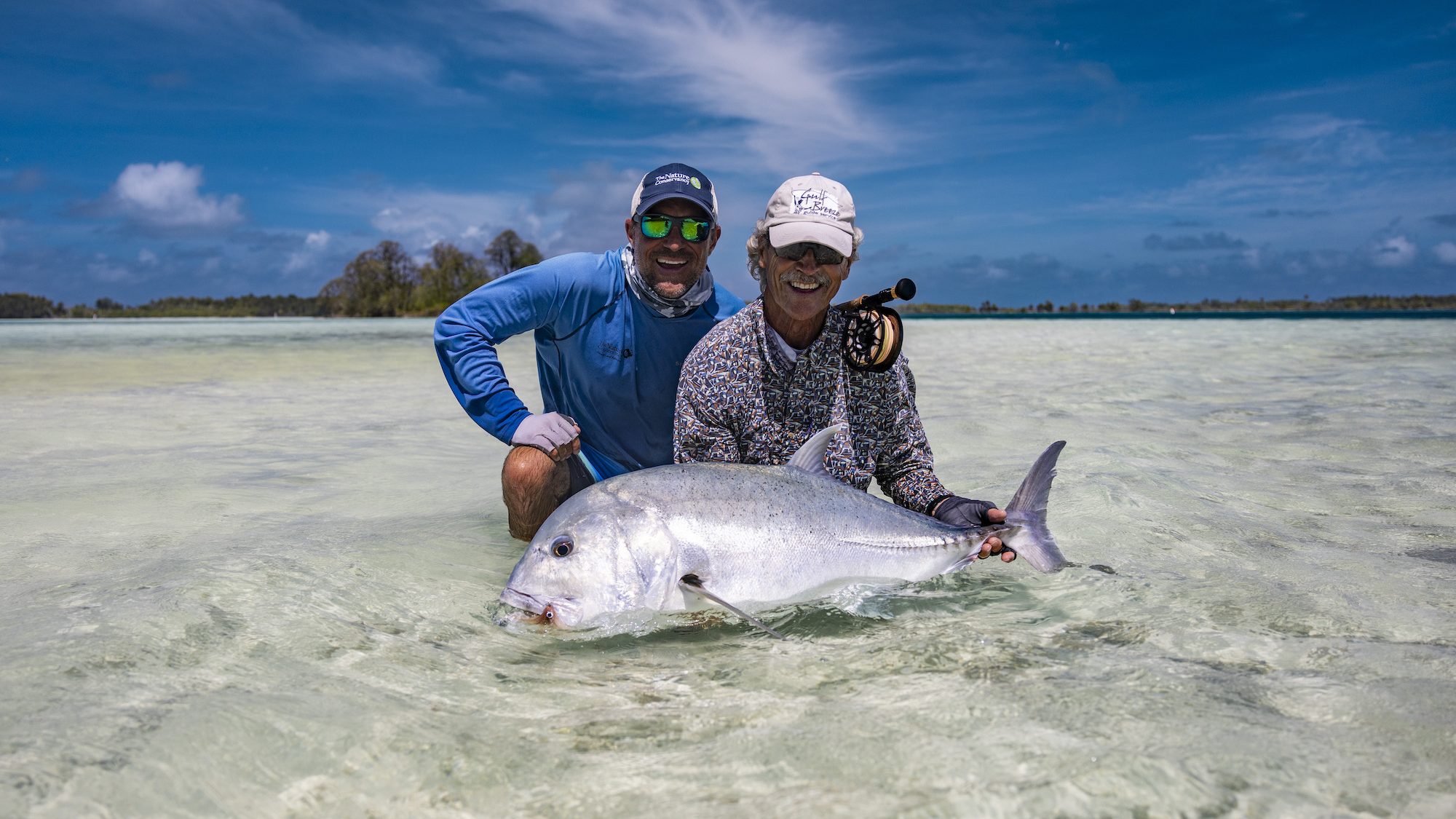 Two men standing in the shallows with a very large fish. 