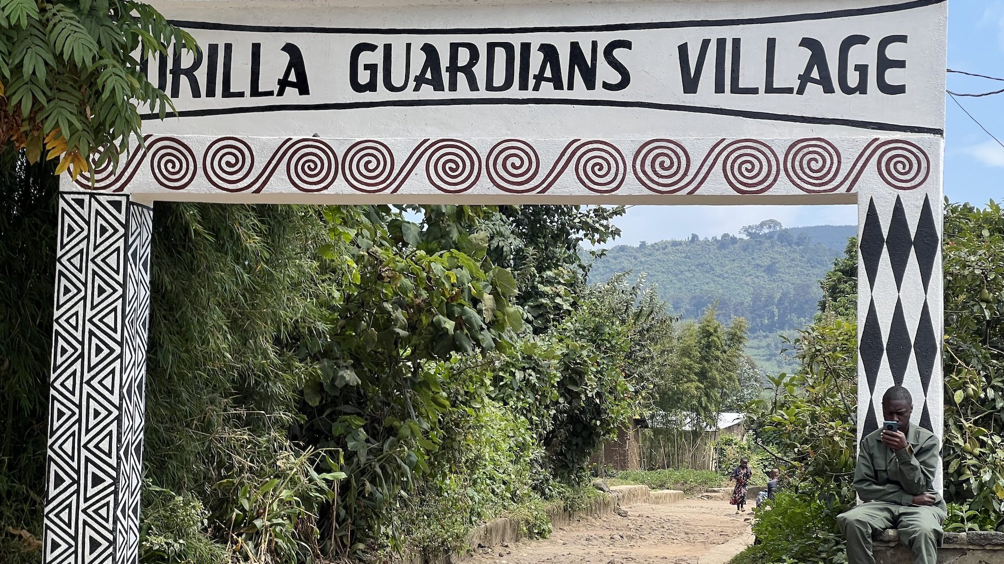 A sign, painted in triangles and swirls, over the road to an African village. 