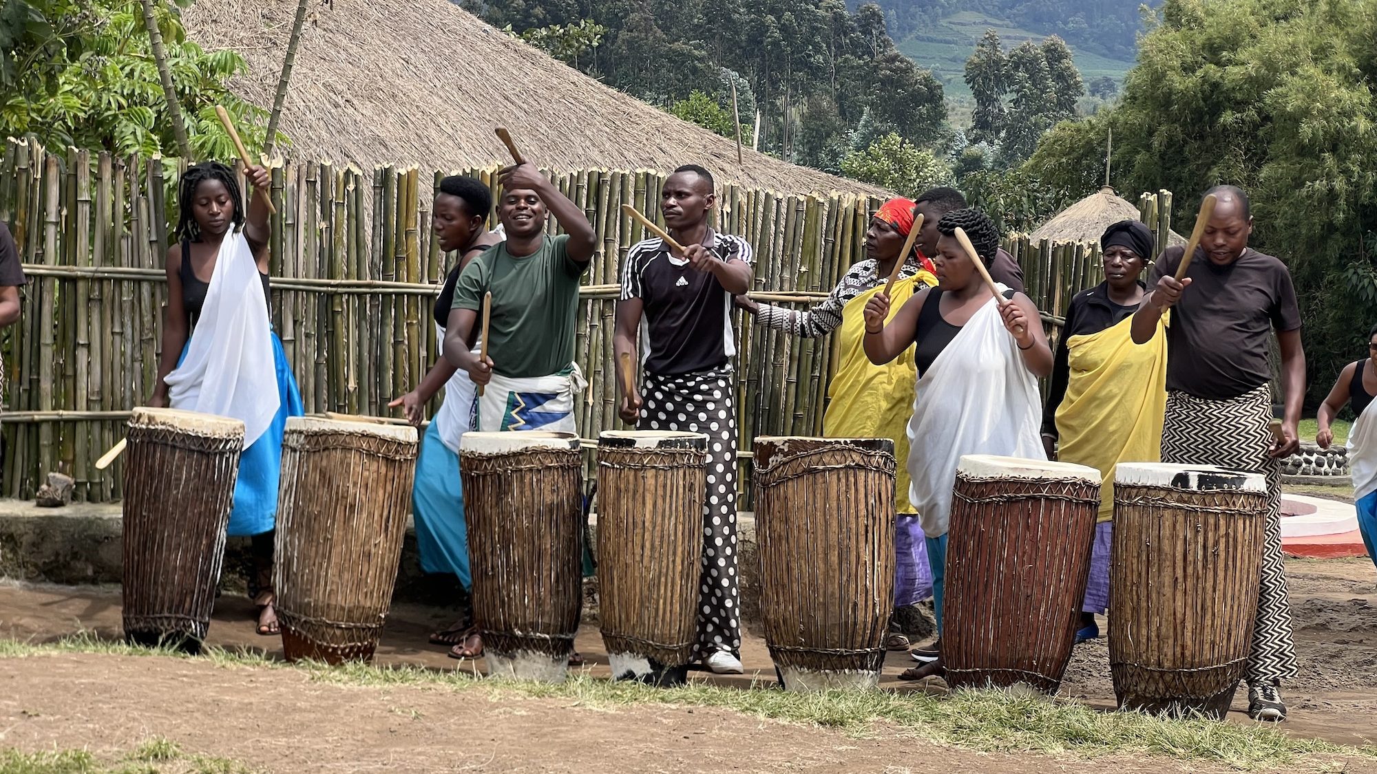 A group of people playing traditional drums outside of a village.  