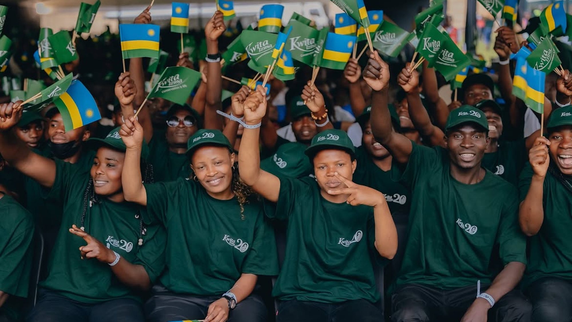 A group of smiling Rwandan teenagers, all holding flags aloft. 