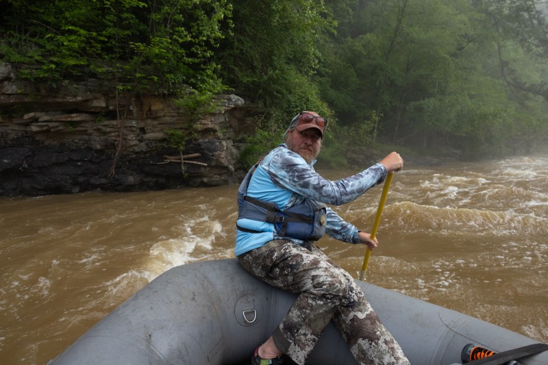 A man rafts along the Locust Fork River near Cleveland, Alabama. He's sitting in the raft and holding a paddle.