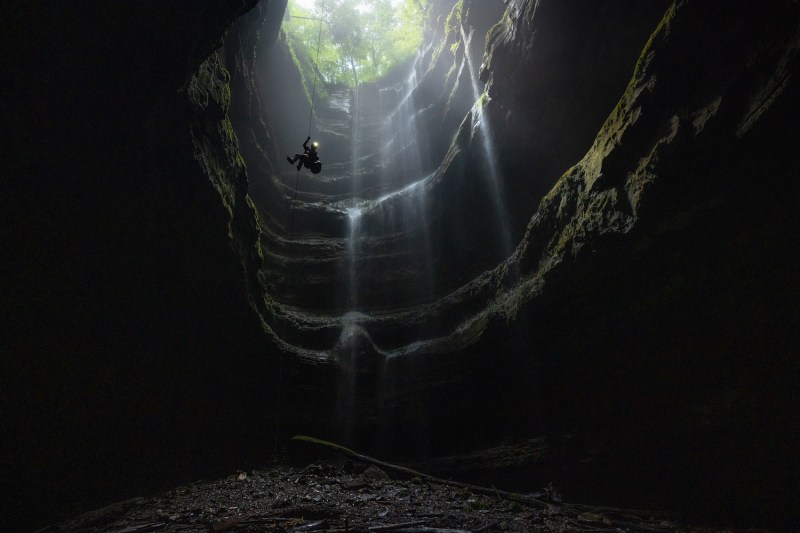 A person descends into the opening of a caves as freshwater from rainfall cascades down the walls.