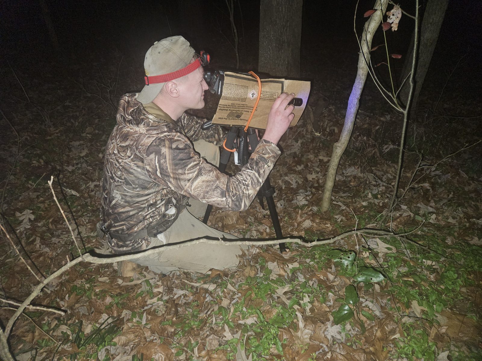 Man in camouflage in the forest at night, using spectrometers and ultraviolet light to image marks on tree trunks.