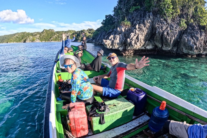 A group of men and women on a boat, with a rocky island in the background.