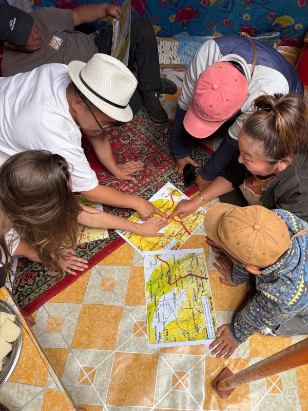 Five people crouched over a map on the floor