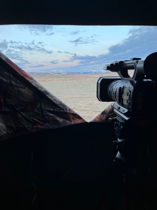 A view looking out from a tent towards mountains. A camera is visible/.