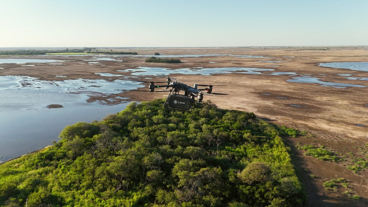 black drone flying over forest, open land and water